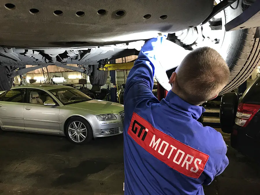 Мастер GTImotors в фирменной куртке осматривает подвеску автомобиля на подъёмнике